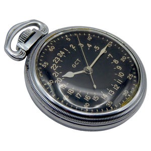 K&ouml;nnte beinhalten: Eine antike Taschenuhr mit schwarzem Zifferblatt und silberfarbenem Geh&auml;use. Das Zifferblatt zeigt Stunden und Minuten an, mit dem Text "GCT". Sie hat eine Schlaufe zum Anbringen einer Kette. Ein zeitloses Design.