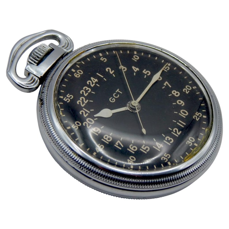K&ouml;nnte beinhalten: Eine antike Taschenuhr mit schwarzem Zifferblatt und silberfarbenem Geh&auml;use. Das Zifferblatt zeigt Stunden und Minuten an, mit dem Text "GCT". Sie hat eine Schlaufe zum Anbringen einer Kette. Ein zeitloses Design.