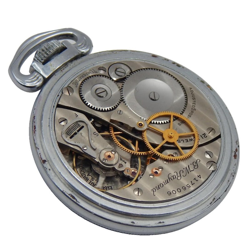 K&ouml;nnte beinhalten: Offene, silberfarbene Taschenuhr mit sichtbaren Zahnr&auml;dern und komplexen mechanischen Komponenten. Das Zifferblatt zeigt das Innenleben, einschlie&szlig;lich Unruh und Zahnr&auml;dern, sowie die Inschrift "B.W. Raymond". Die Uhr hat eine Scharnierschlaufe f&uuml;r eine Kette.