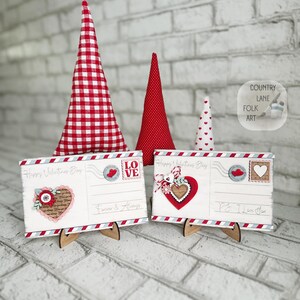 May include: Valentine's Day decorations. Two wooden postcards with heart and floral designs, and three fabric cone trees. The postcards have the text "Happy Valentine's Day", "Forever & Always" and "P.S. I Love You."