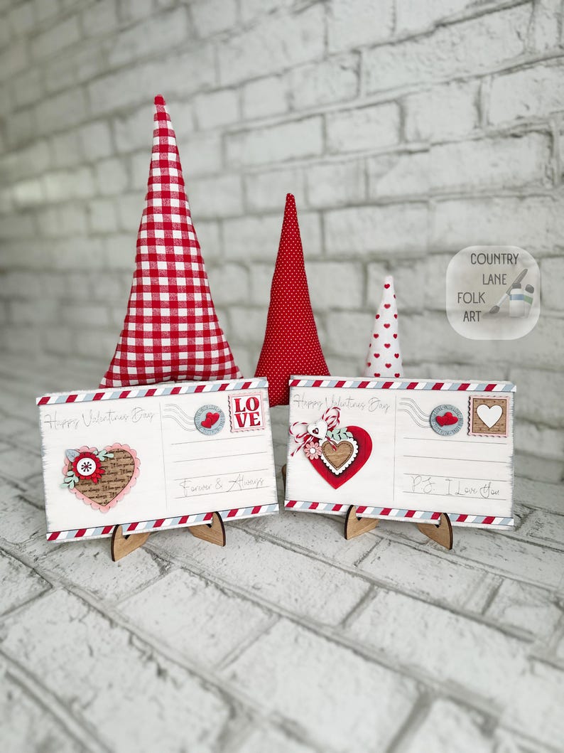 May include: Valentine's Day decorations. Two wooden postcards with heart and floral designs, and three fabric cone trees. The postcards have the text "Happy Valentine's Day", "Forever & Always" and "P.S. I Love You."