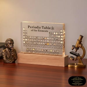 May include: A lit periodic table of elements on a wooden base. The clear acrylic panel displays the table's elements and is illuminated. A bronze Einstein bust and a vintage microscope are also visible.