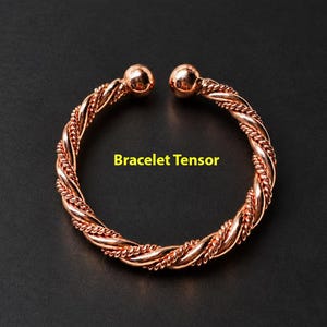 May include: A copper-coloured open cuff bracelet featuring a twisted rope design with a smooth spherical bead at each end. The text Bracelet Tensor is printed in yellow in the centre of the circular opening of the metallic bracelet.