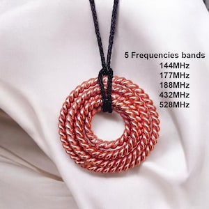 May include: A copper-colored pendant necklace with a circular design made of twisted metal. The necklace hangs from a black cord. Text on the right side reads "5 Frequencies bands" and lists frequencies in MHz.