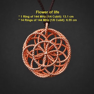 May include: A copper-colored wire pendant featuring a Flower of Life pattern suspended on a dark brown cord. Text states: Flower of life, 1 Ring of 144 MHz (1/4 Cubit): 13.1 cm, 14 Rings of 144 MHz (1/8 Cubit): 6.55 cm. The pendant is circular.