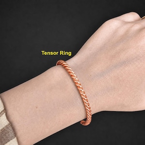 May include: A copper-colored metal bracelet with a twisted rope-like texture. The bracelet is labeled with the yellow text Tensor Ring. The design features a continuous spiral pattern throughout the entire length of the circular metal band.