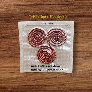 Op de afbeelding: Een witte vierkant met drie rood-witte spiraalvormige ontwerpen, getiteld "Triskelion (Heddeca)". De afmetingen zijn 4 cm. De tekst onderaan luidt "Anti EMF radiation Anti-Wi-Fi protection".