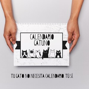 Op de afbeelding: Een witte spiraalgebonden kalender met de tekst "CALENDARIO GATUNO" en een rij zwart-witte cartoonkatten. De kalender bevat ook de tekst "TU GATO NO NECESITA CALENDARIO. TÚ SÍ."