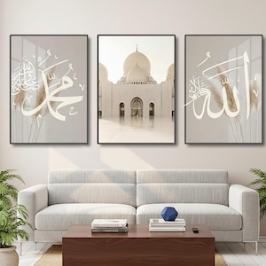 Puede incluir: Tres obras de arte murales enmarcadas. La imagen central es una fotografía de una mezquita blanca. Las otras dos piezas presentan caligrafía blanca sobre un fondo beige, con hierba ornamental seca. Los marcos son negros.