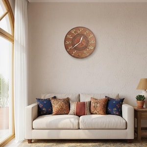 Könnte beinhalten: Eine runde Wanduhr aus Holz mit arabischer Schrift, die über einem cremefarbenen Sofa mit dekorativen Kissen hängt. Die Uhr hat ein dunkelbraunes Zifferblatt mit goldfarbenen arabischen Ziffern und Zeigern. Der Raum hat eine neutrale Farbpalette.