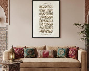 May include: A framed artwork featuring Arabic calligraphy in gold tones against a cream background. The artwork is displayed above a tan sofa adorned with decorative pillows in shades of red, green, and teal. A wooden side table and a lantern are in the foreground.