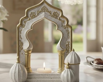 May include: A white and gold decorative candle holder with an arched design. The holder features a small candle, two decorative pillars, and two small decorative domes. The design has a textured, speckled finish.