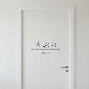 Puede incluir: Una puerta blanca con caligrafía árabe negra y su traducción al inglés. El texto dice: "¡Señor mío! Aumenta mi conocimiento." y "[20:114]" debajo. También se ve un tirador de puerta dorado.