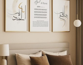 May include: Three framed art prints with gold frames. The prints feature calligraphy and abstract designs in black and beige on a white background. The middle print has the text "Ayet Al Kursi". The artwork is displayed above a bed with pillows.