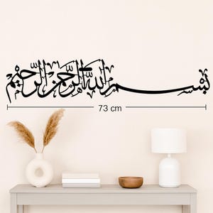 May include: Black wall art featuring Arabic calligraphy script, measuring 73 cm in length. The elegant design is suitable for home decor, adding a touch of cultural artistry to any space. The script is displayed against a neutral background.