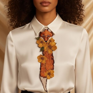 Peut inclure: Chemise blanche avec un motif de renard brodé. Le renard est brun et orange, avec des fleurs jaunes. La chemise a des manches longues et un col classique.