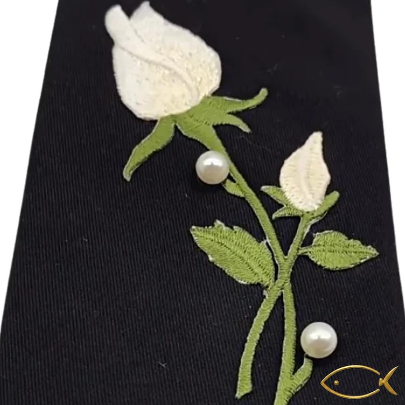 Pu&ograve; includere: Tessuto nero con una rosa e un bocciolo ricamati in bianco, con foglie e stelo verdi. Due perle sono posizionate lungo lo stelo. Un logo di pesce dorato si trova nell'angolo in basso a destra.
