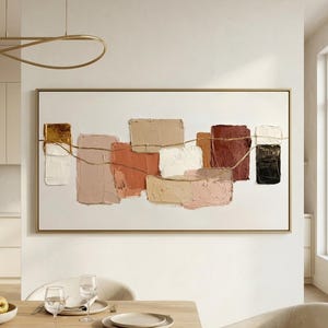 May include: A rectangular wall art piece featuring a series of thick, textured paint blocks in shades of cream, beige, terracotta, rust, and black. A thin, horizontal gold line runs across the centre of the composition, set within a thin gold frame.
