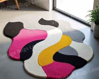 May include: A modern, abstract rug with a unique, organic shape. The rug features a vibrant color palette, including hot pink, yellow, black, white, and gray. The rug is a statement piece for any living space.
