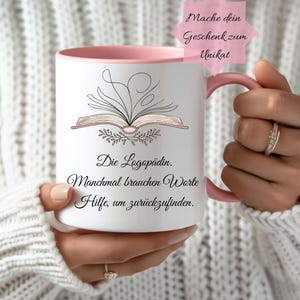 Könnte beinhalten: Weißer Keramikbecher mit rosa Innenraum und Henkel. Der Becher zeigt eine Strichzeichnung eines offenen Buches mit floralen Akzenten und dem Text "Die Logopädin. Manchmal brauchen Worte Hilfe, um zurückzufinden."