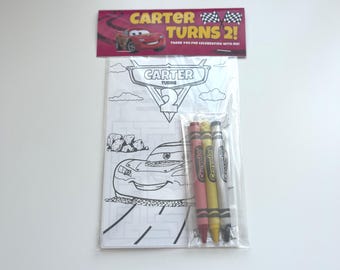 May include: A party favor set featuring a coloring book and crayons. The coloring book has a race car theme with the text "CARTER TURNS 2!". The set includes a pack of four crayons in red, pink, yellow, and gray. The packaging is clear plastic.