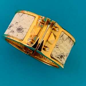 May include: A gold and white hinged bangle bracelet with a snakeskin pattern and clear rhinestones.