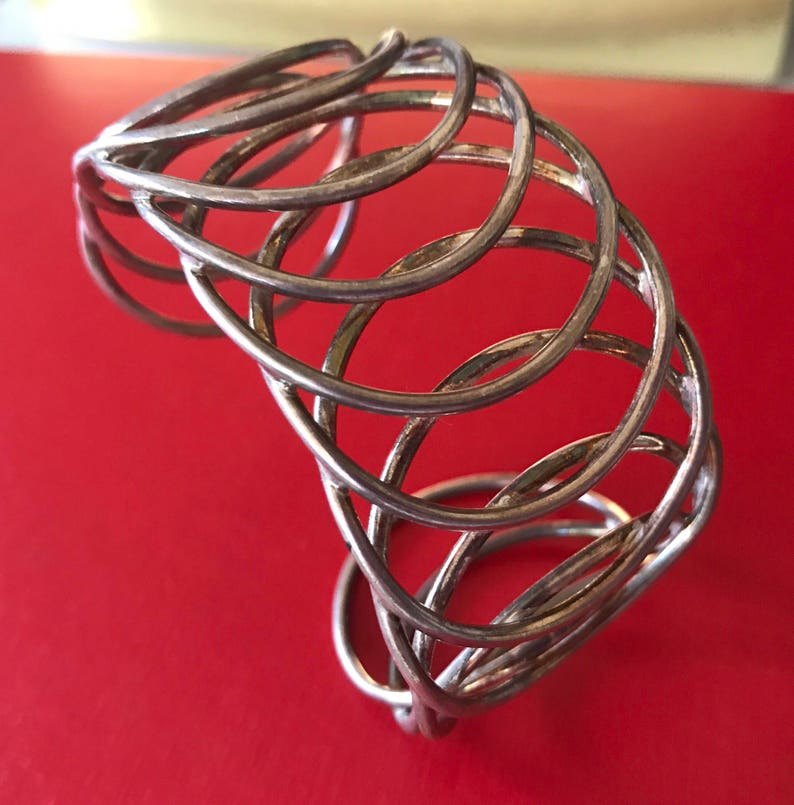 May include: Silver bangle bracelet with a woven design. The bracelet is made of multiple strands of silver wire that are intertwined to create a unique and intricate pattern.