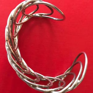 May include: A silver bracelet with a twisted design. The bracelet is made of multiple interlocking rings.