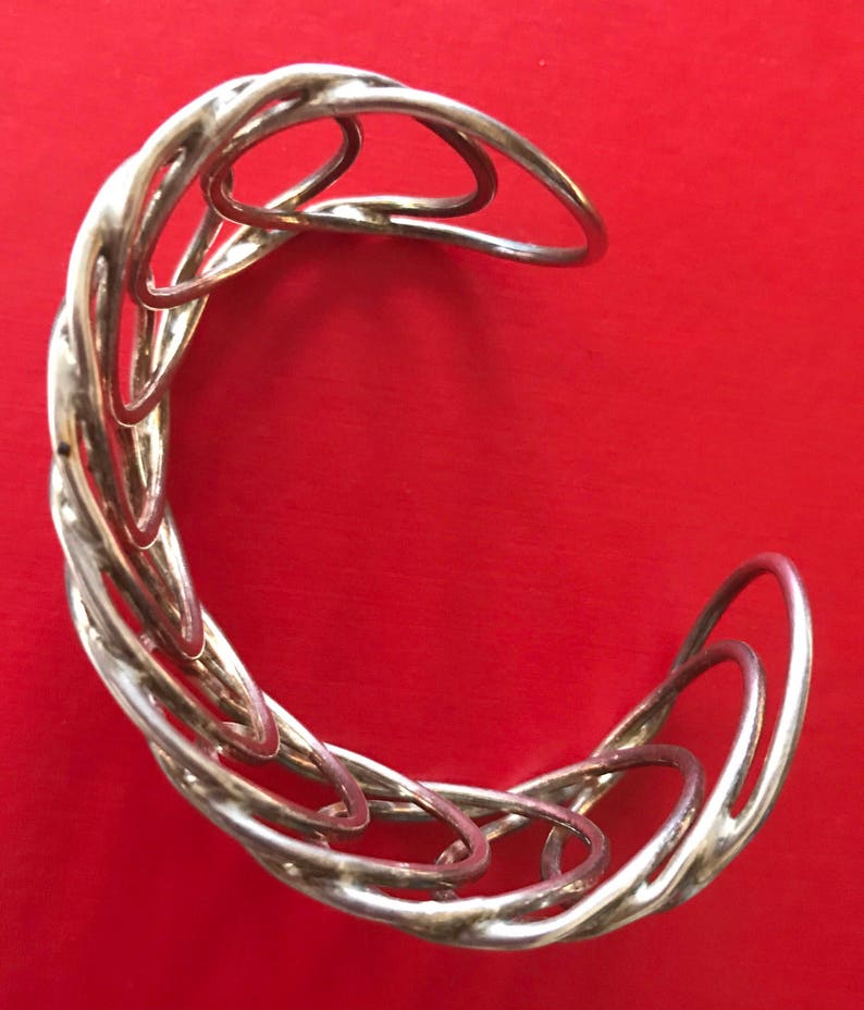 May include: A silver bracelet with a twisted design. The bracelet is made of multiple interlocking rings.