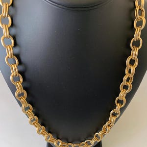 May include: A gold chain necklace with a thick, linked design. The chain is displayed on a black mannequin bust.
