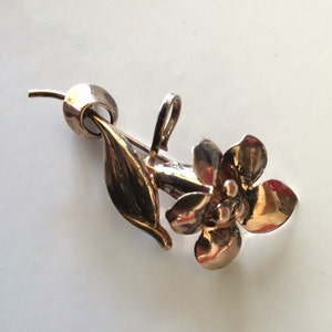 May include: A gold-toned flower brooch with a single leaf. The flower has five petals and a center with three small round accents.