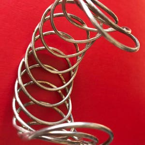 May include: A silver metal bracelet with a unique, multi-layered design. The bracelet is made of several intertwined rings, creating a textured and intricate look.