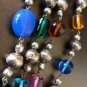 May include: A multi-strand necklace with a variety of beads, including gold, blue, green, pink, and orange. The beads are strung on a silver chain.