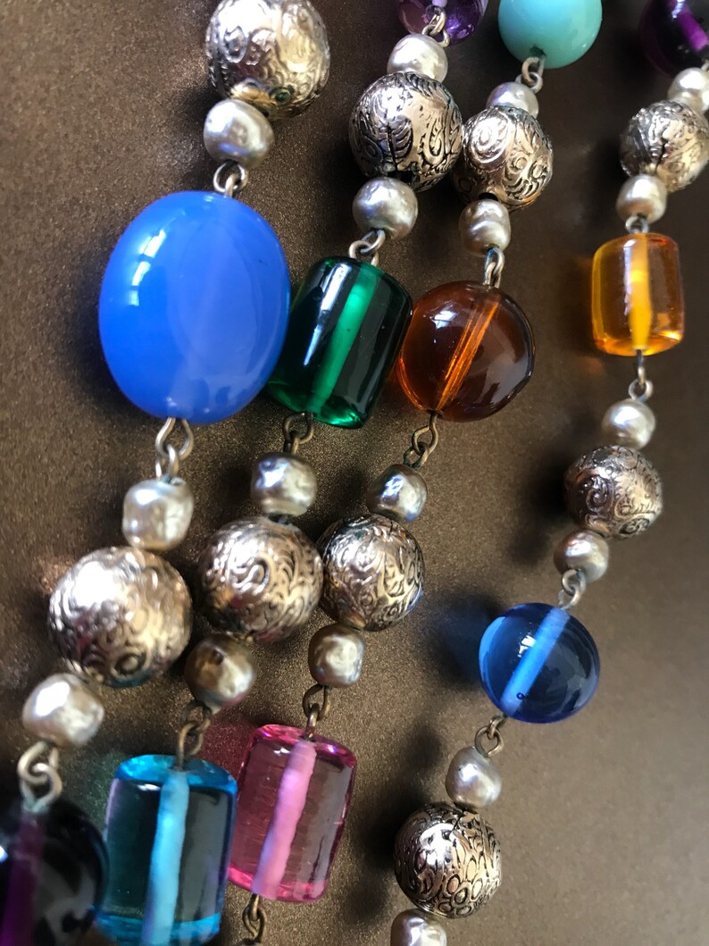 May include: A multi-strand necklace with a variety of beads, including gold, blue, green, pink, and orange. The beads are strung on a silver chain.