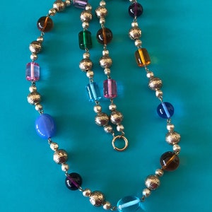 May include: A colorful beaded necklace with silver round beads and various colored glass beads, including blue, green, purple, pink, and orange. The necklace has a silver clasp.