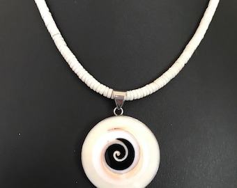 May include: A white shell pendant necklace with a black and white spiral design. The necklace is made of white beads and has a silver clasp.