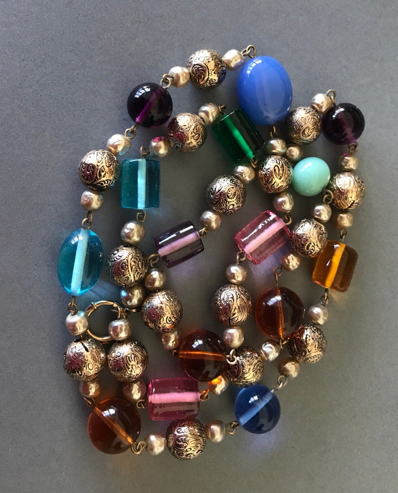 May include: A colorful beaded necklace with a mix of round and rectangular glass beads in shades of blue, green, purple, pink, and amber. The necklace is strung on a silver chain with decorative metal beads.