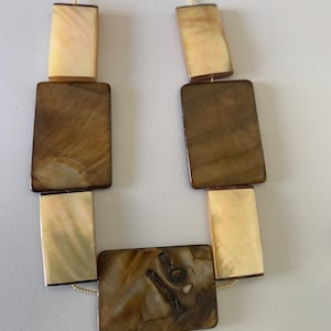 May include: A gold chain necklace with brown and cream rectangular shell beads. The necklace is made of natural materials and has a unique, organic look.