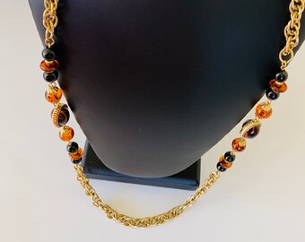 May include: A gold chain necklace with brown and black beads. The beads have a gold trim.