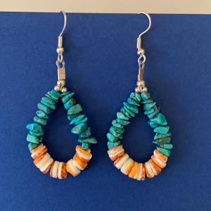 May include: A pair of turquoise and orange stone dangle earrings with silver hooks. The earrings are made of small, irregular shaped stones.