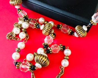 May include: A gold chain necklace with white pearls, gold beads, clear crystal beads, and black beads.