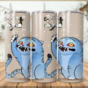 Puede incluir: Tres vasos de acero inoxidable con un dise&ntilde;o de gato de dibujos animados. El gato es azul con ojos amarillos y la boca abierta. El fondo es de color beige claro con un p&aacute;jaro en una rama.