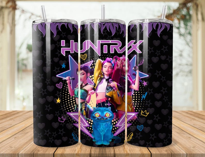 Puede incluir: Un vaso negro con tapa y pajita moradas. El vaso presenta un gr&aacute;fico de tres mujeres con micr&oacute;fonos, la palabra "HUNTRAX" y un gato azul. El fondo tiene estrellas, corazones y puntos.