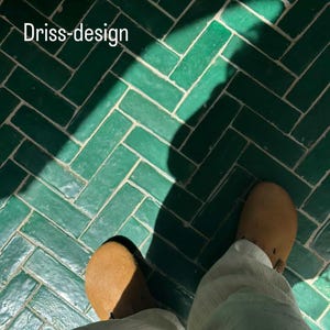 May include: A person wearing light brown clogs and white pants stands on a green tiled floor. The floor has a herringbone pattern. The text "Driss-design" is visible in the upper left corner.