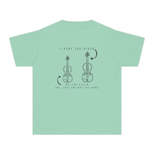 May include: A pale green t-shirt featuring the text "I PLAY THE VIOLA" above two black line drawings of stringed instruments. Below the drawings is the text "NOT THE VIOLIN (NO, THEY ARE NOT THE SAME)".