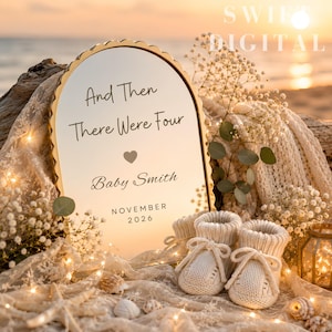 Puede incluir: Un espejo arqueado con marco dorado festoneado que presenta el texto And Then There Were Four, un icono de corazón, Baby Smith y NOVEMBER 2026. Junto al espejo hay un par de patucos de punto color crema, flores blancas y conchas marinas.