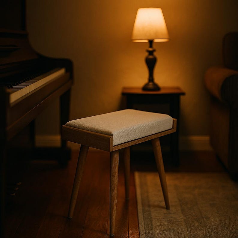 Puede incluir: Un taburete de piano de madera con un asiento rectangular acolchado en beige claro. Tiene un marco de madera y cuatro patas anguladas. El taburete est&aacute; en una habitaci&oacute;n con un piano, una l&aacute;mpara y una alfombra.