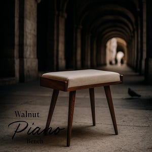 Puede incluir: Un banco de piano de nogal con un asiento rectangular y acolchado en un color neutro. El banco tiene un marco de madera oscura y patas anguladas. El texto "Walnut Piano Bench" se muestra en la parte inferior izquierda.