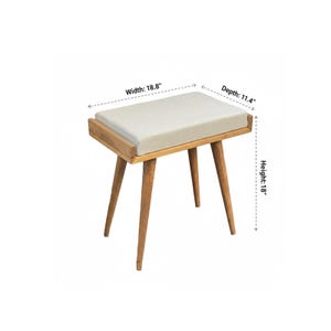 Puede incluir: Un taburete de madera con un asiento rectangular y acolchado. El asiento es de color beige claro, y el marco y las patas son de color madera natural. El taburete mide 45.7 cm de alto, 47.8 cm de ancho y 29 cm de profundidad. Las patas est&aacute;n inclinadas hacia afuera.