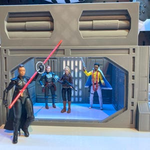 May include: A Star Wars action figure diorama featuring four figures. One figure holds a red lightsaber, while others wield weapons. The figures are inside a grey, industrial-style structure with a blue-lit interior.